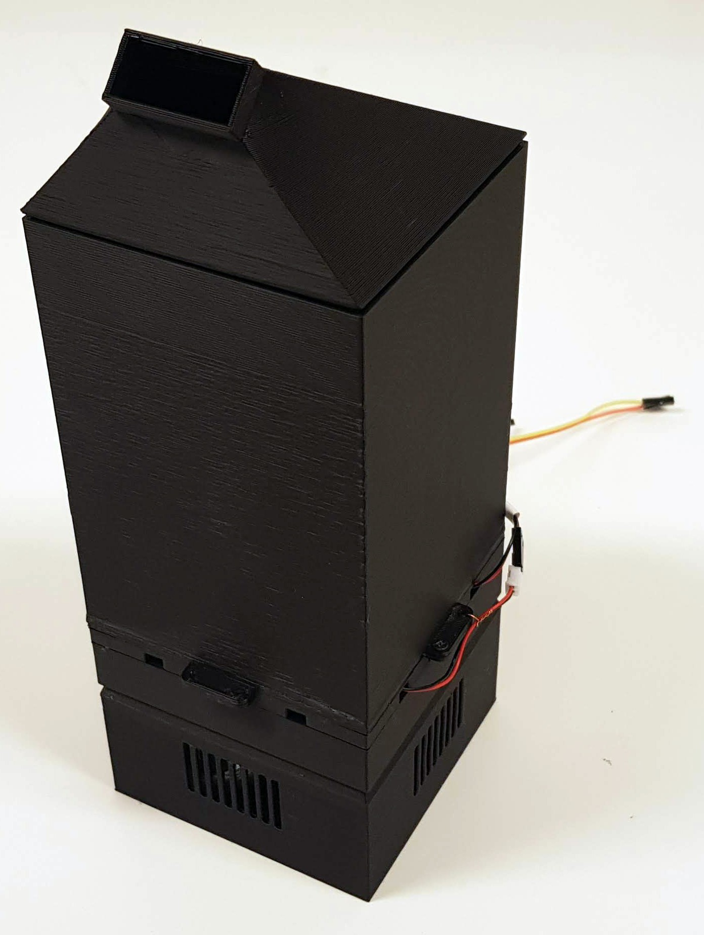 The Scentony device fully assembled, standing. It's a black 3d printed box with groves at the bottom and a slightly tilted funnel attachment at the top – Liam Aljundi
